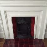 Glossy deep red ceramic hearth tiles forming a fireplace hearth in front of a decorative fire opening.
