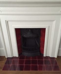 Glossy deep red ceramic hearth tiles forming a fireplace hearth in front of a decorative fire opening.