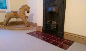Glossy red ceramic hearth tiles laid in front of a decorative cast-iron fireplace, forming the fireplace hearth.