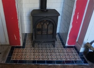 Patterned ceramic hearth tiles in front of a wood-burning stove, with decorative circles and dark border tiles forming the fireplace hearth.
