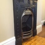 Yellow ceramic hearth tiles laid in a neat square grid, forming a traditional fireplace hearth in front of a dark wooden surround and cast-iron firebox.