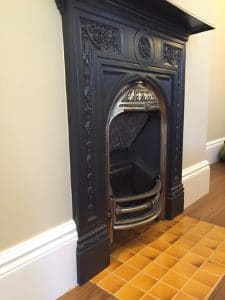 Yellow ceramic hearth tiles laid in a neat square grid, forming a traditional fireplace hearth in front of a dark wooden surround and cast-iron firebox.