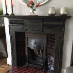 Fireplace with a dark wooden surround and a burgundy and red rectangular hearth tiles laid in a brick pattern.
