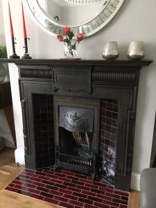 Fireplace with a dark wooden surround and a burgundy and red rectangular hearth tiles laid in a brick pattern.